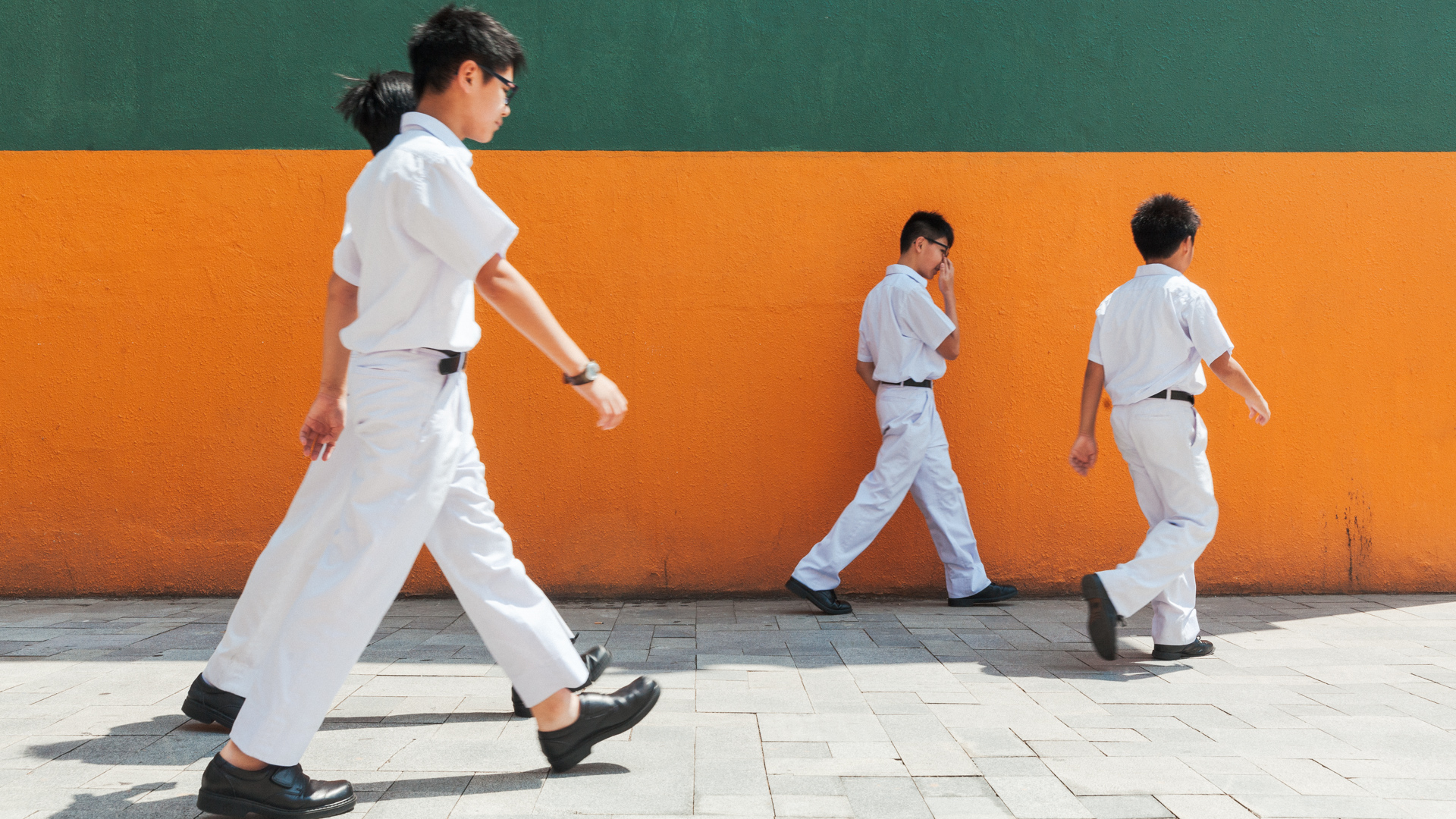 Schoolboys walking past an orange wall